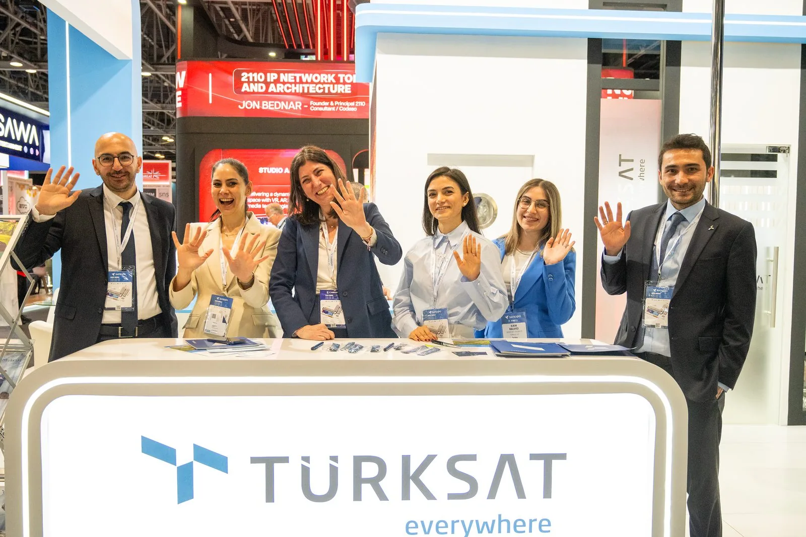 Technology representatives at a broadcast and satellite exhibition stand.