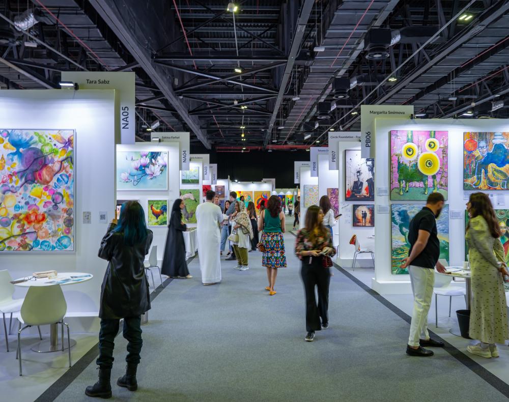 Visitors walk through a World Art Dubai gallery aisle with colourful framed artwork.